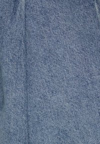 Tela de mezclilla en azul claro con una textura suave y un patrón de sarga clásico, que exhibe sutiles variaciones en color y matices.