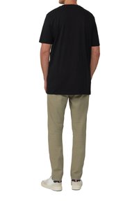 Zwart katoenen t-shirt met een ronde hals, gecombineerd met lichtbeige linnen broek en witte sneakers, gezien vanuit de achterkant.