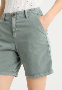 Shorts en coton vert clair à texture lisse, dotés d'une poche avant, d'une fermeture par bouton et d'un ourlet retourné.
