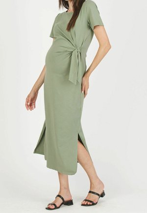 Robe longue vert olive avec un détail noué sur le côté, manches courtes et fentes hautes sur les côtés. Tissu lisse et doux qui épouse le corps.