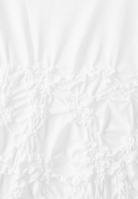 Tissu blanc avec texture froncée formant un motif floral et géométrique en relief sur toute la surface.