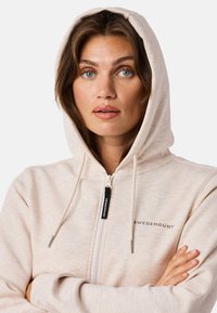 Light beige zip-up hoodie with a fleece texture, adjustable hood, and a small logo "SWEDEMOUNT" on the chest. Features silver hardware.
