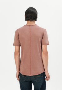 Kurzärmliges, rostfarbenes T-Shirt mit Rundhalsausschnitt, abgerundetem Saum und sichtbaren Nähten entlang der Mitte des Rückens.