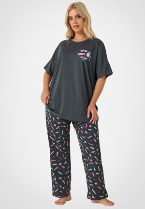 Kvinde iført mørkegrå kortærmet top med teksten "søvn er sødt" og mønstrede pyjamasbukser med farverige slikdesigns.