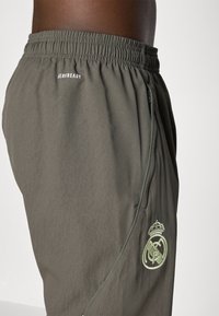 Dark green athletic shorts with an elastic waistband, featuring "AEROREADY" text and an embroidered logo with a crown on the side.