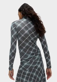 Maglietta a maniche lunghe, aderente, di colore grigio con motivo a quadri blu petrolio e bianco. Tessuto morbido, scollatura rotonda e dettagli arricciati sul retro.