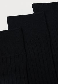 Három pár fekete zokni bordás textúrával. Minden zokni a tetején kötött mintázattal és sima testtel rendelkezik, ami kényelmet és megfelelő illeszkedést biztosít.