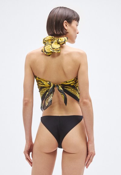 Črni bikini z rumeno ruto z vzorcem, pripeto zadaj, ki poudarja gladko teksturo in halter dizajn. Gola hrbtna stran in prilegajoč spodnji del.