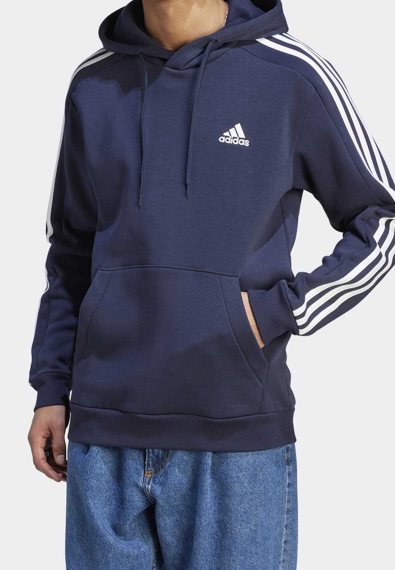 Laivastonsininen hupullinen collegepaita, jossa valkoinen Adidas-logo, sivuraidat, kiristysnauha ja etutasku. Valmistettu pehmeästä, teksturoidusta kankaasta.