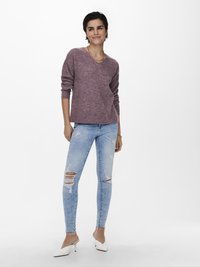 V-Ausschnitt, mauve Strickpullover mit gerippten Bündchen, kombiniert mit hellblauen, ausgewaschenen Skinny Jeans mit Rissen und weißen, hohen Mules.