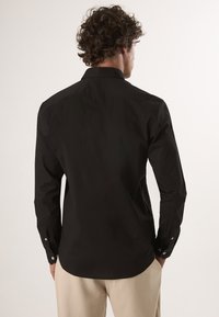 Schwarzes Langarmshirt mit geradem Saum, Rückenpasse und geknöpften Manschetten. Aus glattem Baumwollstoff, mit klassischem Kragen-Design.