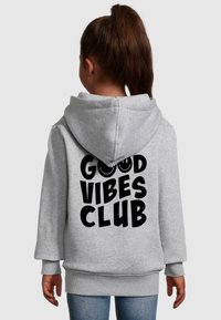 Sivá mikina s kapucňou a predným vreckom, vo voľnom strihu, s veľkým čiernym nápisom "GOOD VIBES CLUB" na zadnej strane. Bavlnený materiál, mäkká textúra.