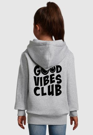 Grijze hoodie met een voorzak, oversized pasvorm en grote zwarte tekst "GOOD VIBES CLUB" op de rug. Katoenen materiaal, zachte textuur.