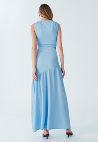 Gaiši zilas krāsas maksi kleita ar piegulošu augšdaļu, teksturētu audumu un izplešamu svārku. Tai ir augsts kakla izgriezums un gluda siluets.