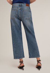 Jeans de denim de corte amplio, en un lavado medio, con una cintura alta, costuras en contraste y dos bolsillos traseros. Presenta un parche de cuero marrón en la cintura.