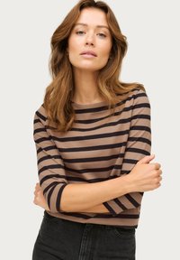 Braun und schwarz gestreiftes Langarmshirt mit U-Boot-Ausschnitt und figurbetontem Schnitt, aus weichem Stoff. Kombiniert mit hochgeschnittenen dunklen Jeans.