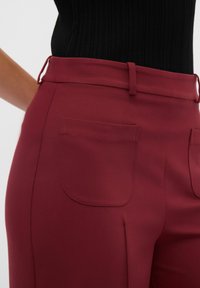 Bordeauxkleurige broek met een slim fit, gemaakt van een gladde stof. Kenmerkt zich door een subtiele zak en ceintuurlussen, ontworpen met een stijlvolle afwerking.
