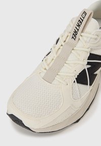 White athletic shoe with mesh and suede materials, featuring black accents, a textured overlay, and prominent lacing system with a tab.
