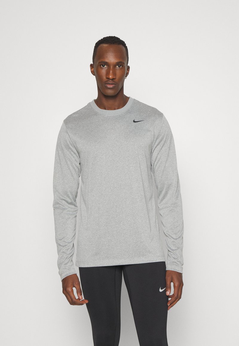 T-shirt de sport à manches longues en tissu gris clair, avec un col rond et un logo Nike noir sur le côté gauche de la poitrine. Matériau doux et texturé.