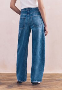 Modré rifle z denimu s voľným strihom a s vysokým pásom. Majú päť vreciek, ošúchaný lem a textúrovanú tkaninu so slabým vyblednutím.