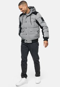 Grå dunjakke med sorte accenter, der har hætte, frontknapper og to store lommer; glat tekstur med et quiltet design.