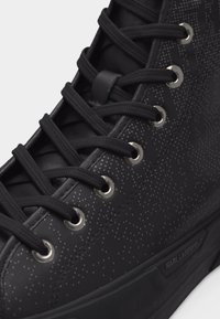Μαύρο ψηλό αθλητικό παπούτσι με μαύρα κορδόνια, ασημένιες τρύπες και διακριτικό πουα μοτίβο στο πλάι με την επωνυμία «Karl Lagerfeld» στη σόλα.