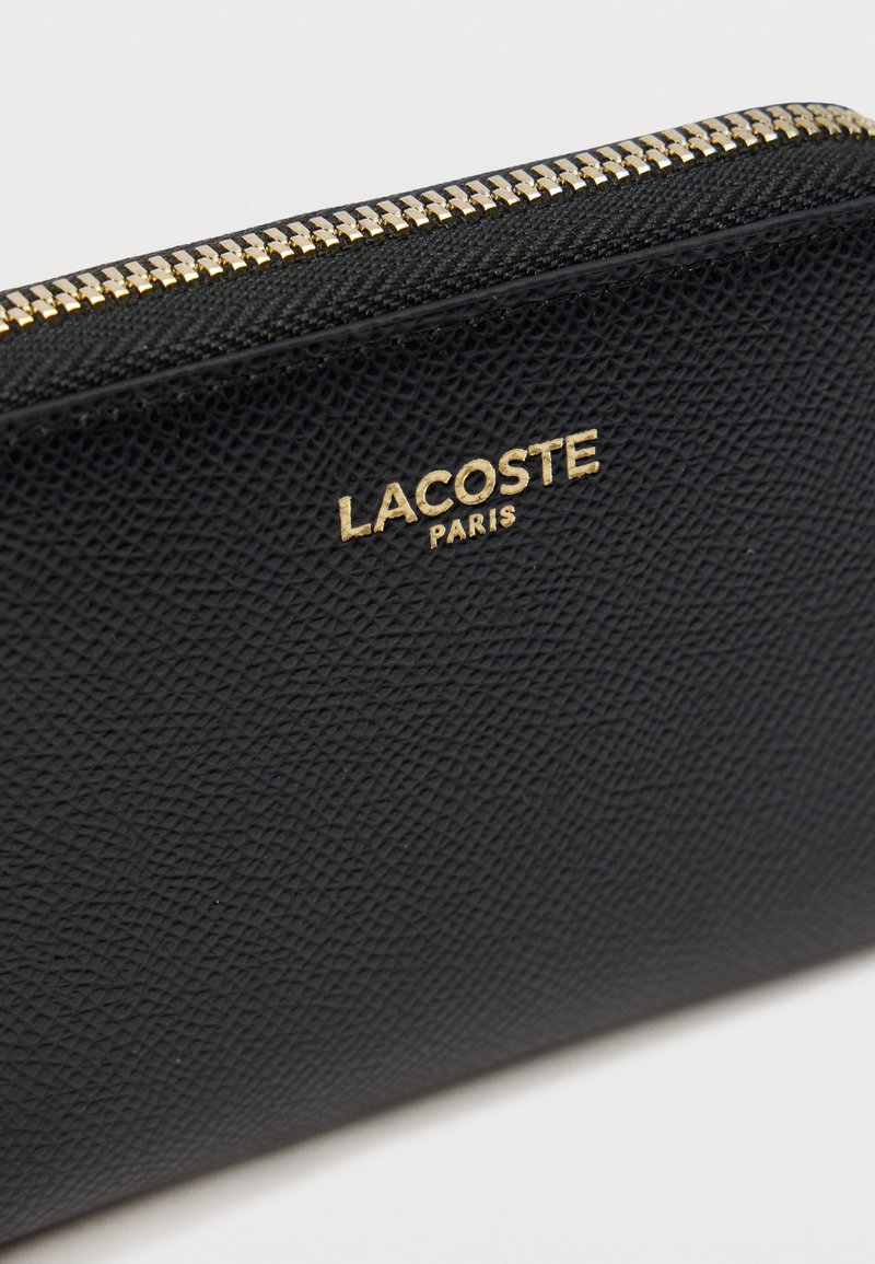 Zwart gestructureerd lederen portemonnee met gouden ritssluiting en gouden Lacoste Paris-logo aan de voorkant.