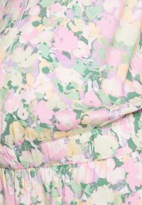 Tecido com padrão floral apresentando tons suaves de rosa, amarelo e verde com uma superfície ligeiramente texturizada; detalhe de cintura franzida visível.