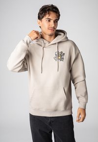 Beige hoodie met een voorzak, trekkoorden en een grafisch ontwerp op de linkerborst. Heeft een ontspannen pasvorm en geribbelde manchetten.