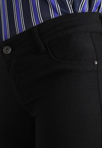 Czarne dżinsy z denimu z klasycznym paskiem w talii, przednią kieszenią i detalem z srebrnym guzikiem. Gładka tekstura i dopasowany krój.