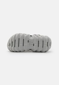 Grå fottøy med ribbet, strukturert design og ventilasjonshull. Lett materiale med rund såle for komfort. Distinkt form.