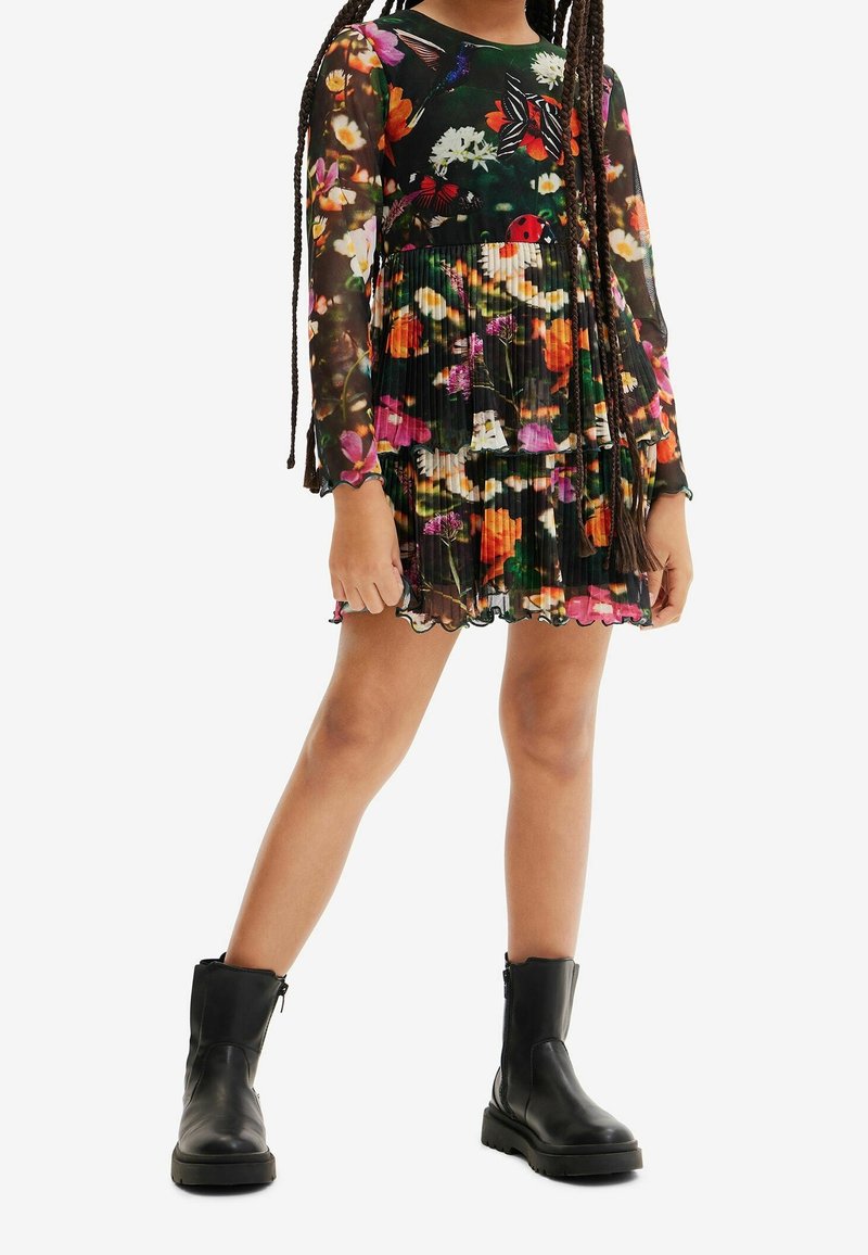 Robe à manches longues à fleurs avec un design plissé, présentant un fond noir et des fleurs colorées. Associée à des bottines en cuir noir.