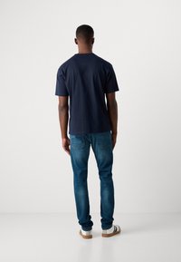 Camiseta de algodón azul marino de manga corta, combinada con unos jeans ajustados. Los jeans presentan un diseño clásico de cinco bolsillos y costuras sutiles.
