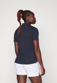 Polo azul-marinho com mangas curtas, detalhe na gola e fenda lateral; combinado com calções brancos. Tecido texturizado e respirável.