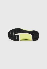 Semelle de chaussure avec une base en caoutchouc noir texturé ornée de motifs en zigzag, une semelle intermédiaire blanche proéminente et un accent jaune vif sur le bord supérieur.