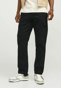 Pantaloni cargo negri, cu multiple buzunare laterale, cu un croi drept și din material de bumbac, asortați cu adidași gri și albi.