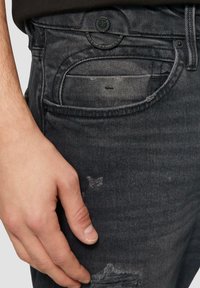 Czarne dżinsy o standardowym kroju, z widoczną kieszenią i akcentami na szwach oraz delikatnymi przetarciami w okolicy dołu.