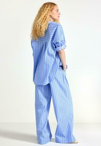 Lys blå stribet oversized skjorte parret med matchende wide-leg bukser, der har foldede ærmer og sidelommer. Glat stofstruktur.