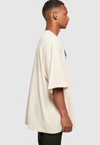 Creme oversized t-shirt lavet af bomuld med korte ærmer og rund halsudskæring. Har et sort logo på forsiden. Lige pasform.