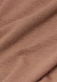 Tissu doux et texturé dans une teinte rose chaud et doux. Motifs de tricot visibles avec de légères variations d'ombre et de détails de tissage.
