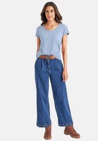 Lichtblauwe t-shirt met korte mouwen, gecombineerd met hoge taille wijdvallende donkere spijkerbroek en bruine veterschoenen. Bruine riem met decoratieve gesp.