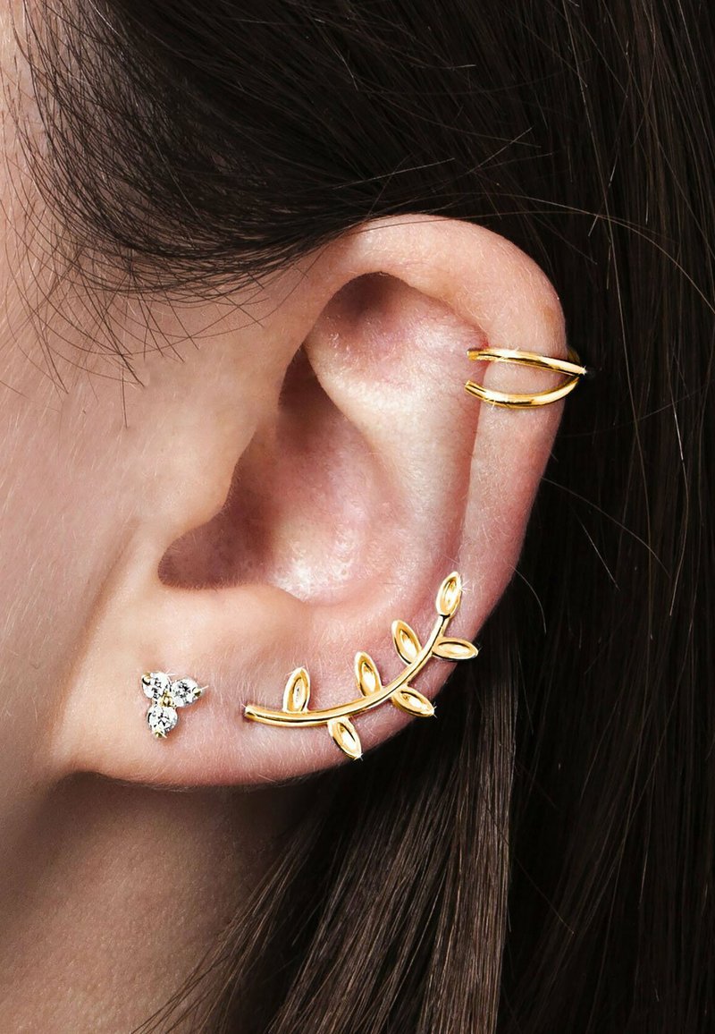 Goldfarbener, blattförmiger Ohr-Cuff und ein kleiner Ohrstecker mit drei Steinen, vor einem Hintergrund aus Haut und braunem Haar.