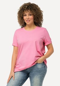 T-shirt di cotone rosa con maniche corte arrotolate e girocollo, abbinato a jeans in denim blu chiaro. Texture liscia, vestibilità rilassata.