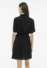 Juoda trumpomis rankovėmis suknelė su apykakle, diržo juosmeniu ir laisvu kirpimu, pagaminta iš minkštos, tekstūruotos medžiagos, siekiančios iki kelių.