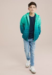 Vadderad zip-jacka i gradient teal med huva, tillsammans med en marinblå skjorta och ljusblå jeans. Skor: vita sneakers med grå detaljer.