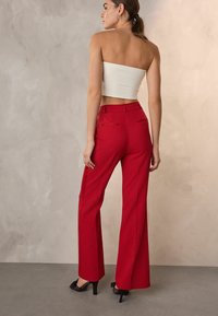 Punaiset leveälahkeiset housut, jotka on valmistettu teksturoidusta kankaasta, korkealla vyötäröllä ja tuplataskuilla takana. Yhdistetty valkoiseen olkaimettomaan toppiin ja mustiin korollisiin kenkiin.