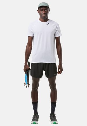 T-shirt de sport blanc à manches courtes, short noir, chaussettes noires et chaussures de course grises. Tient des bâtons de randonnée bleus, design minimaliste.