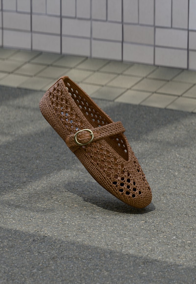 Chaussure plate tissée marron à bout rond, design perforé et bride décorative avec boucle dorée, reposant sur une surface texturée.