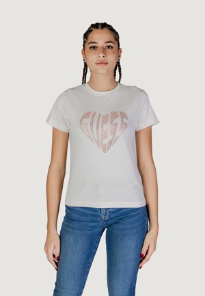 T-shirt bianco in cotone con logo a forma di cuore in rosè metallico. Collo tondo classico e maniche corte. Indossato con jeans in denim blu.