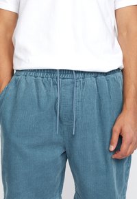 Blauwe corduroy broek met een elastische tailleband en trekkoord. Verticale ribbels, zijzakken en een ontspannen pasvorm.